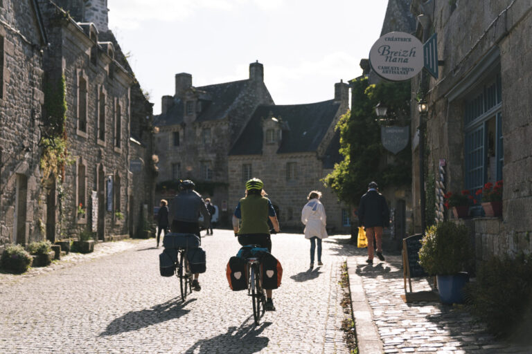 2 cyclistes dans le centre de Locronan, soleil de face